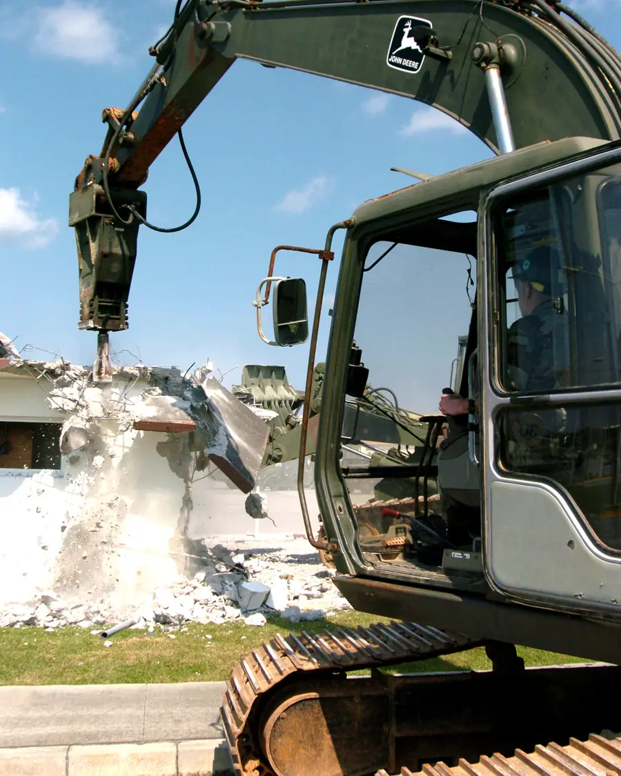 Excavator with a hydraulic breaker attachment smashing through a concrete block wall