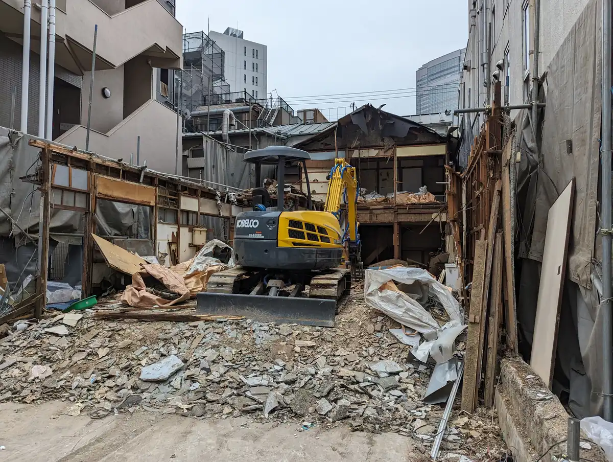 Compact excavator working through the rubble of a partly demolished single-family house